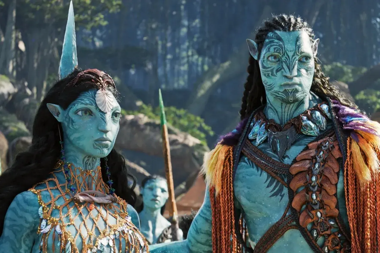 Neytiri i Jake w strojach Na'vi, czekają na premierę Avatar 3. Ich twarze zdobią plemienne wzory, a w tle widać fragmenty pandoriańskiego lasu.