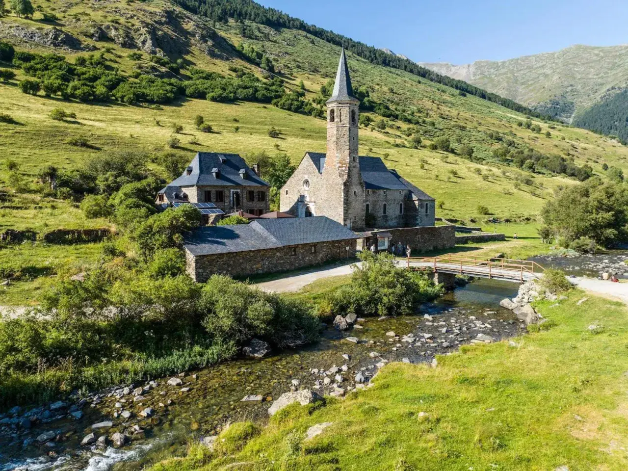 El santuari de Montgarri, una joya arquitectónica de piedra, se alza sereno junto a un arroyo cristalino, rodeado de verdes laderas montañosas.