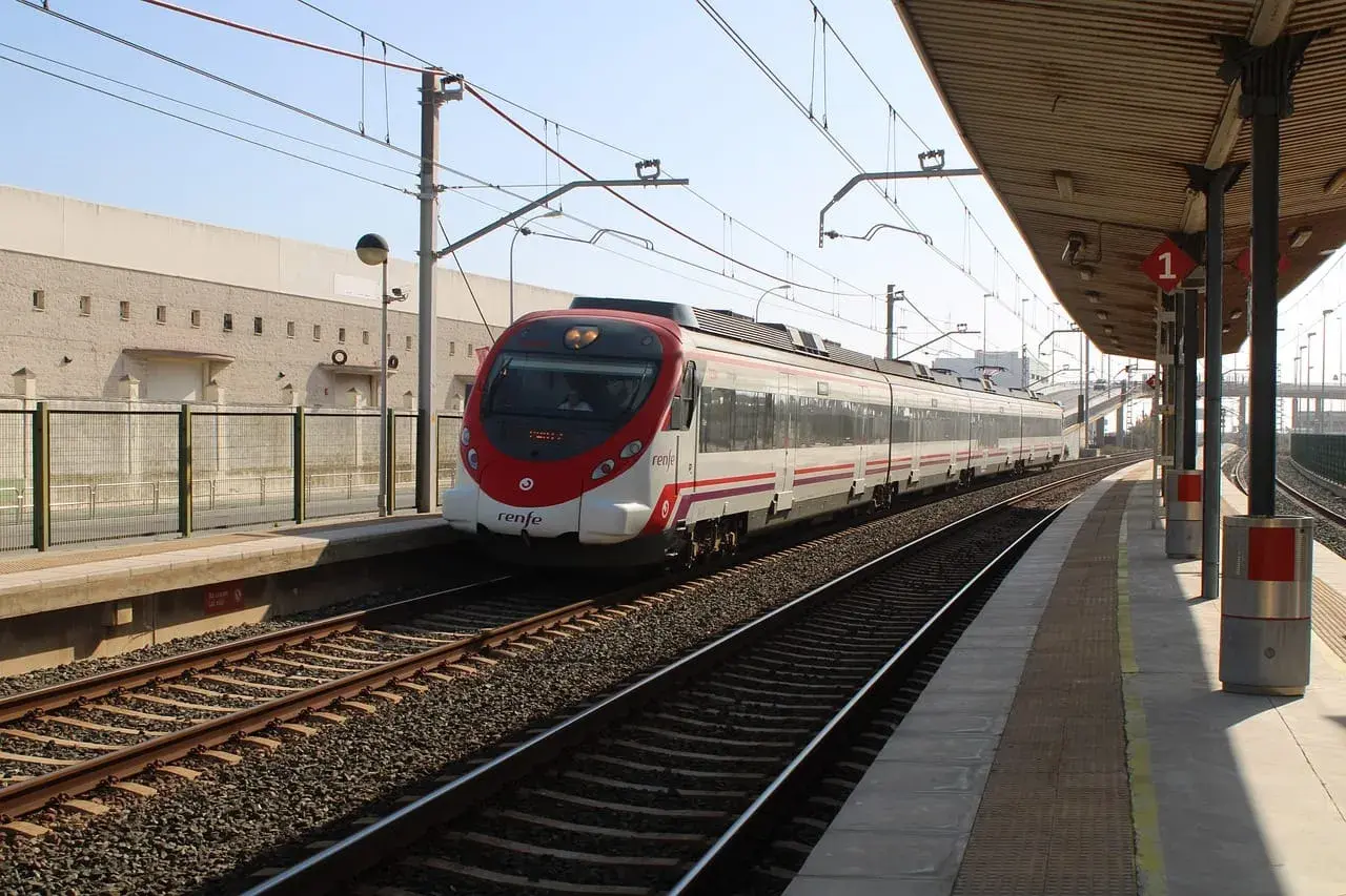 Nowoczesny pociąg Renfe z czerwonym przodem stoi na stacji. W tle budynek i peron.