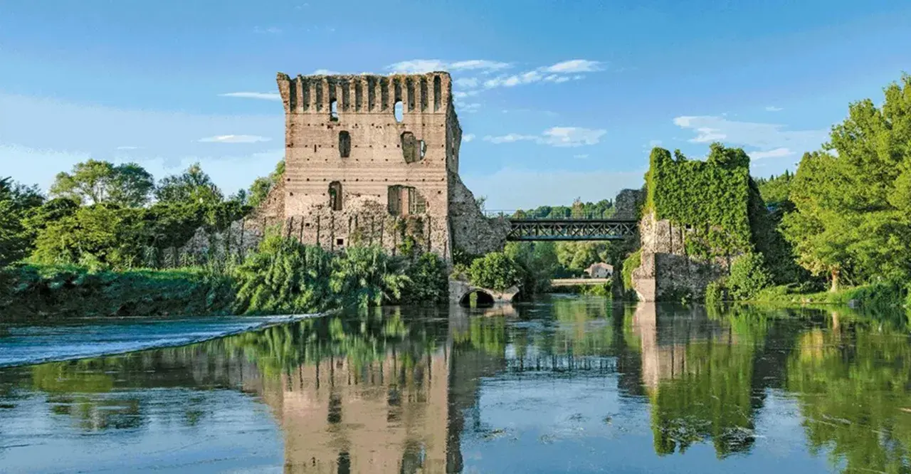 Rovine di un castello e un ponte sul Mincio, con riflessi sull'acqua calma.