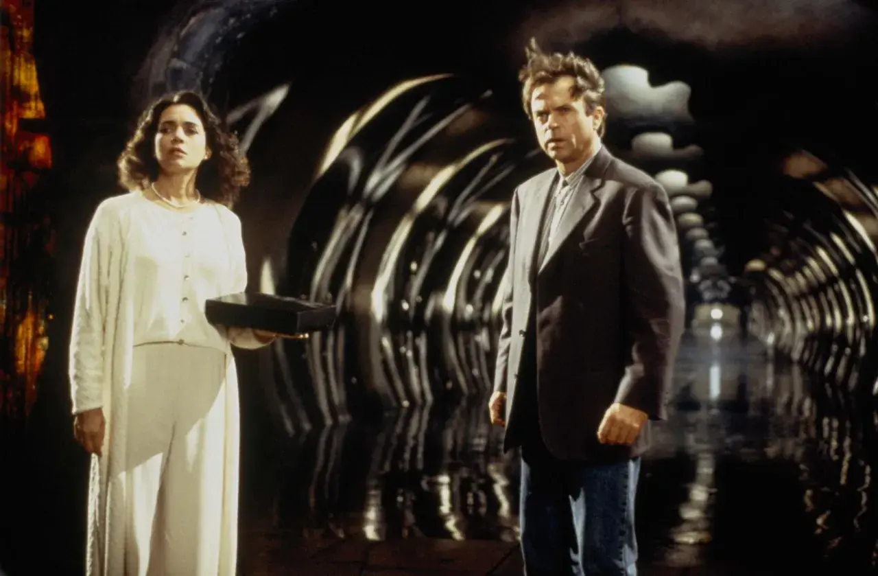 Uomo e donna in un tunnel futuristico. Lei tiene una scatola nera, forse il seme della follia, il cui significato è ancora ignoto.