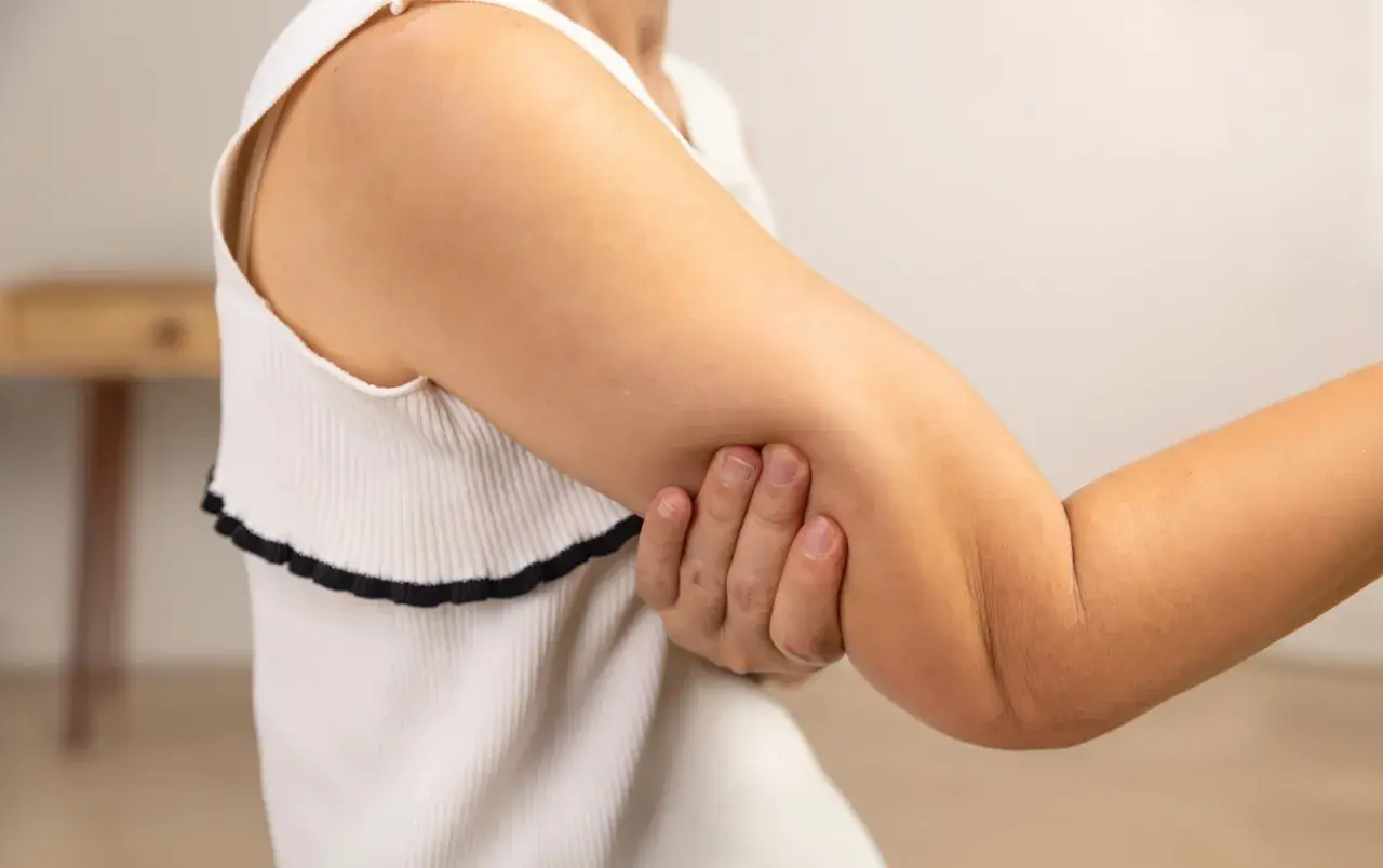 En person håller om sin armbåge, som om det gör ont i båda armarna.