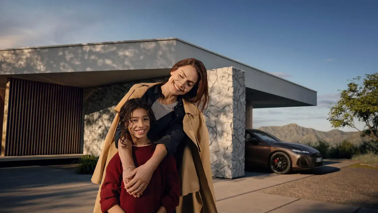 Madre e hija sonríen frente a una casa moderna con un Mercedes. El mantenimiento de tu Mercedes es clave para estos momentos.