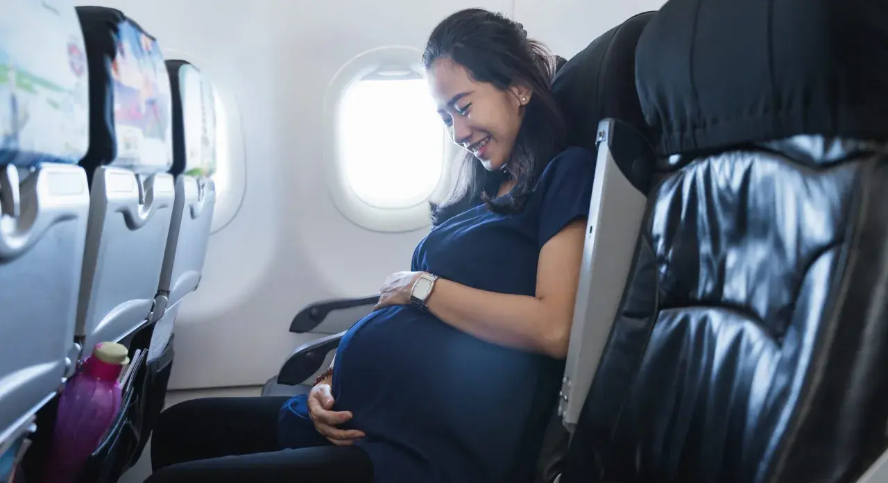 Glad gravid kvinna ler och håller sin mage medan hon sitter i ett flygplan.