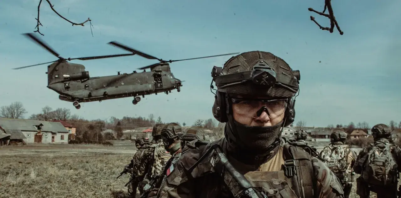 Żołnierze w pełnym rynsztunku, gotowi do akcji podczas szkolenia wojskowego. W tle widać helikopter transportowy.