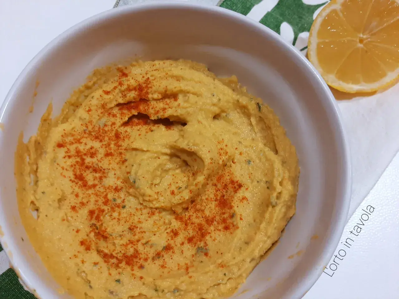 Hummus di ceci senza tahina, cremoso e spolverato di paprika, pronto per essere gustato con una fetta di limone.