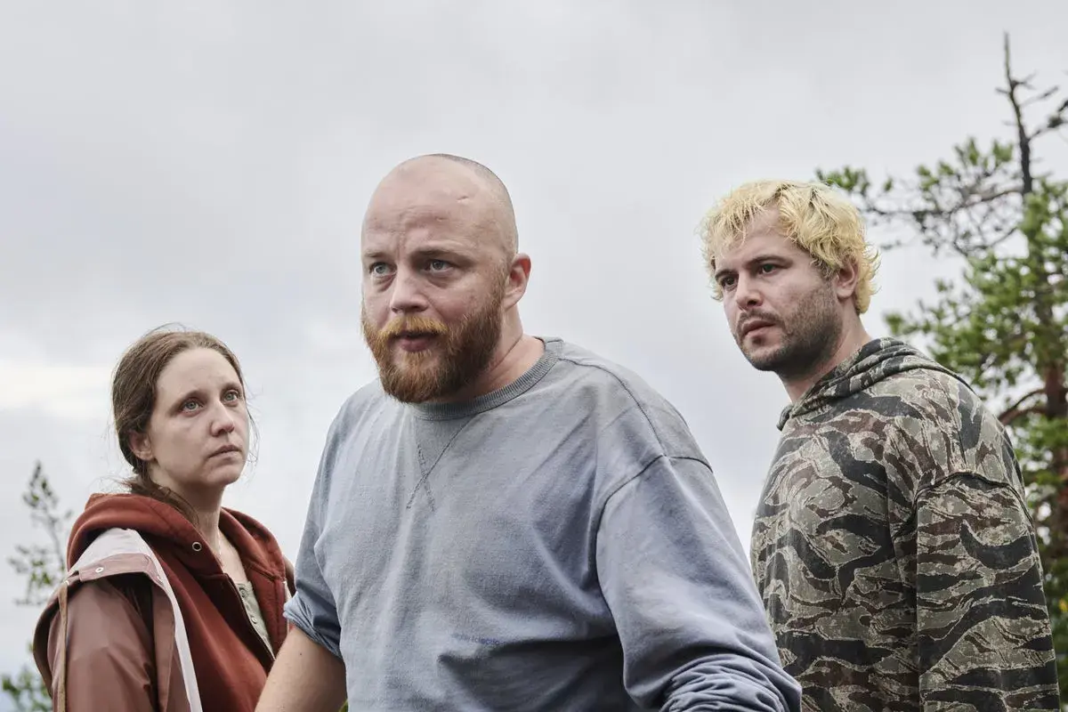 Tre personer, en kvinna och två män, står utomhus i en skogsmiljö. Det är en scen från "Vargasommar del 2".