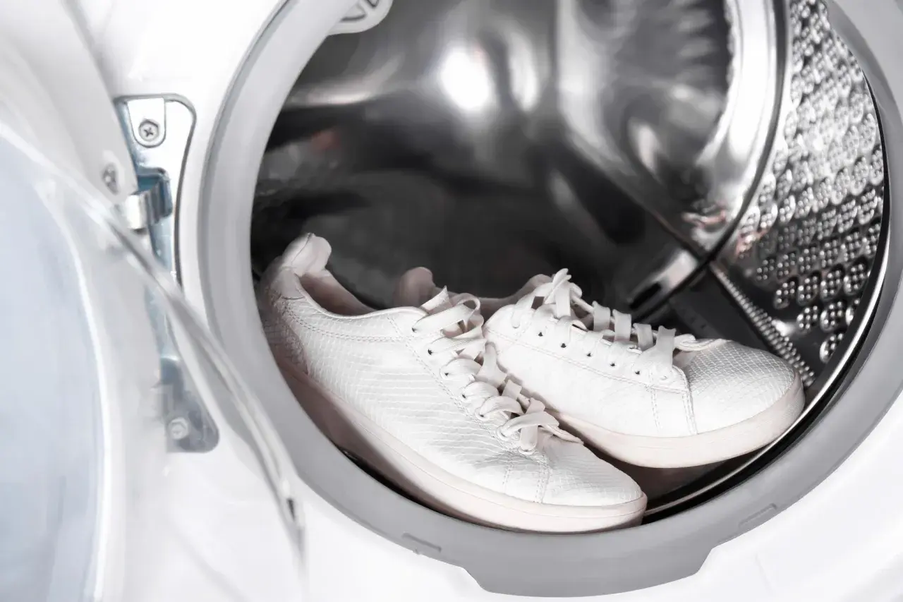 Weiße Sneaker warten im Inneren einer Waschmaschine auf ihren Einsatz.