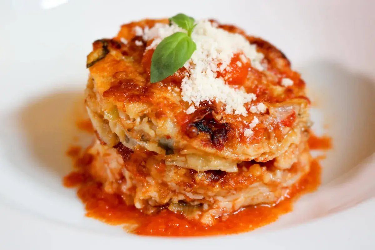 Parmigiana di alici, un tortino stratificato con pesce, verdure e pomodoro, guarnito con basilico e parmigiano.