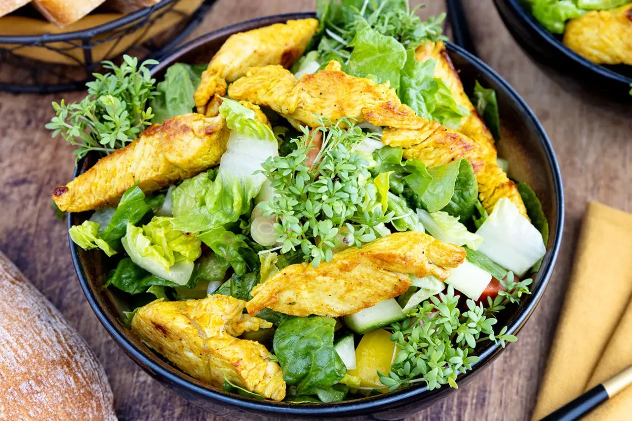 Ein frischer Salat mit knackigem Grün, Gurken und gelben Paprikastücken, garniert mit würzigen Putenstreifen und Kresse.