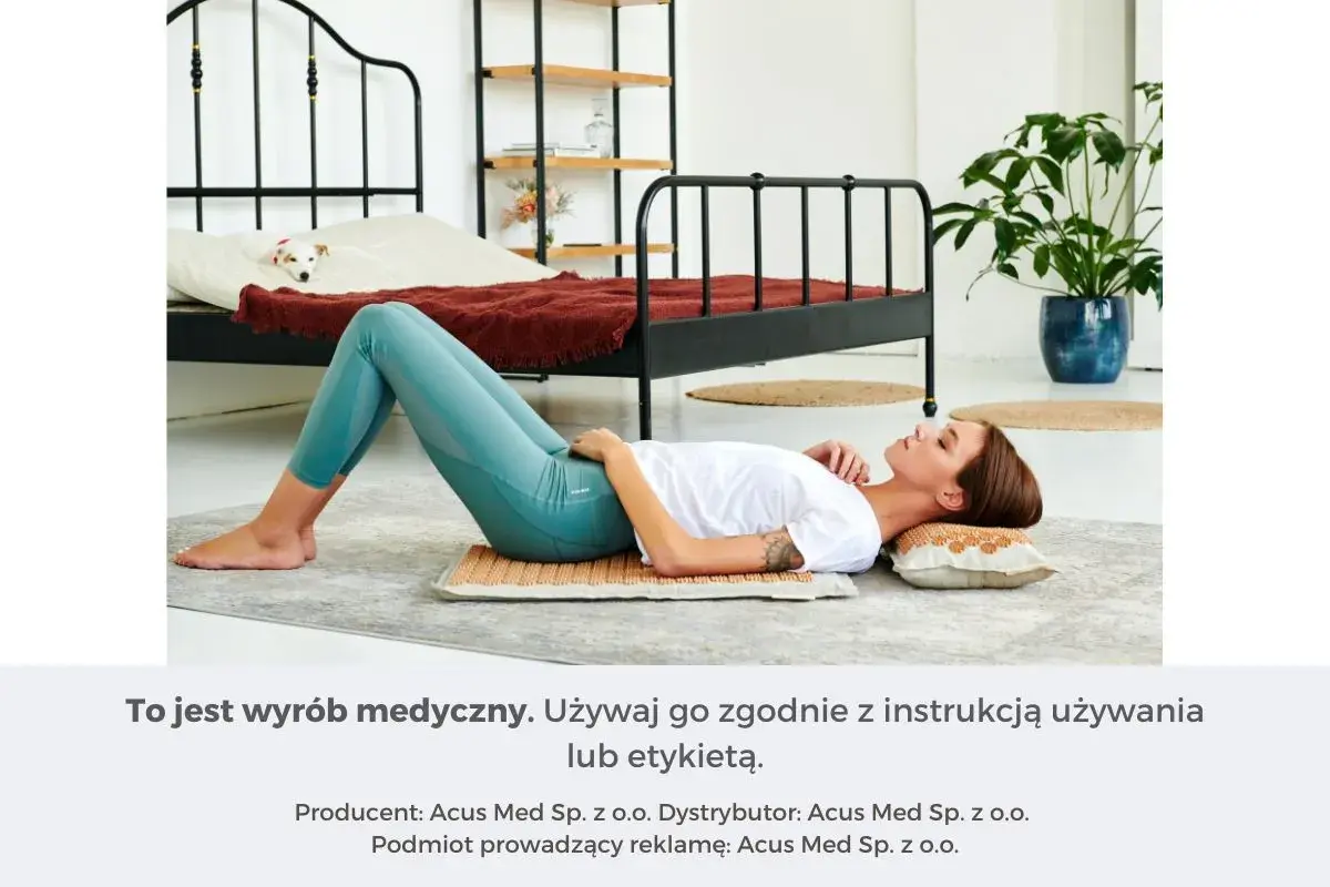 Kobieta leży na macie akupresurowej, która zapewnia masaż uda. W tle łóżko z psem.
