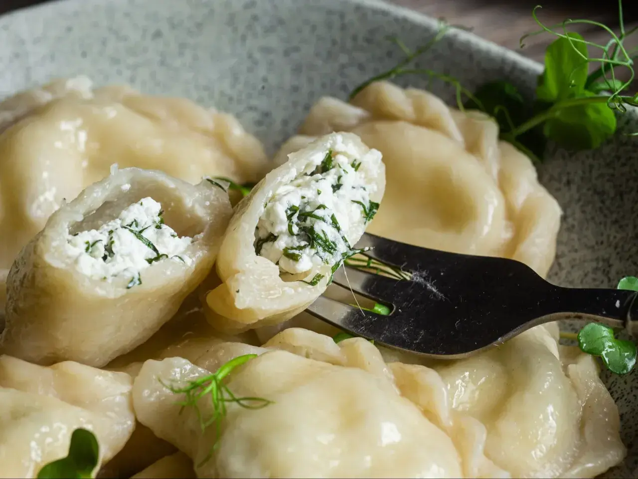Pyszne pierogi z serem i zieloną natką, jeden uchwycony widelcem, gotowy do skosztowania.