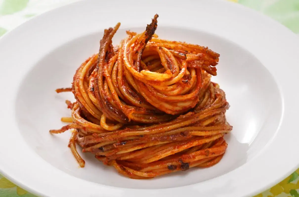 Spaghetti all'assassina, lekko przypieczone, w intensywnym sosie pomidorowym, ułożone na białym talerzu.