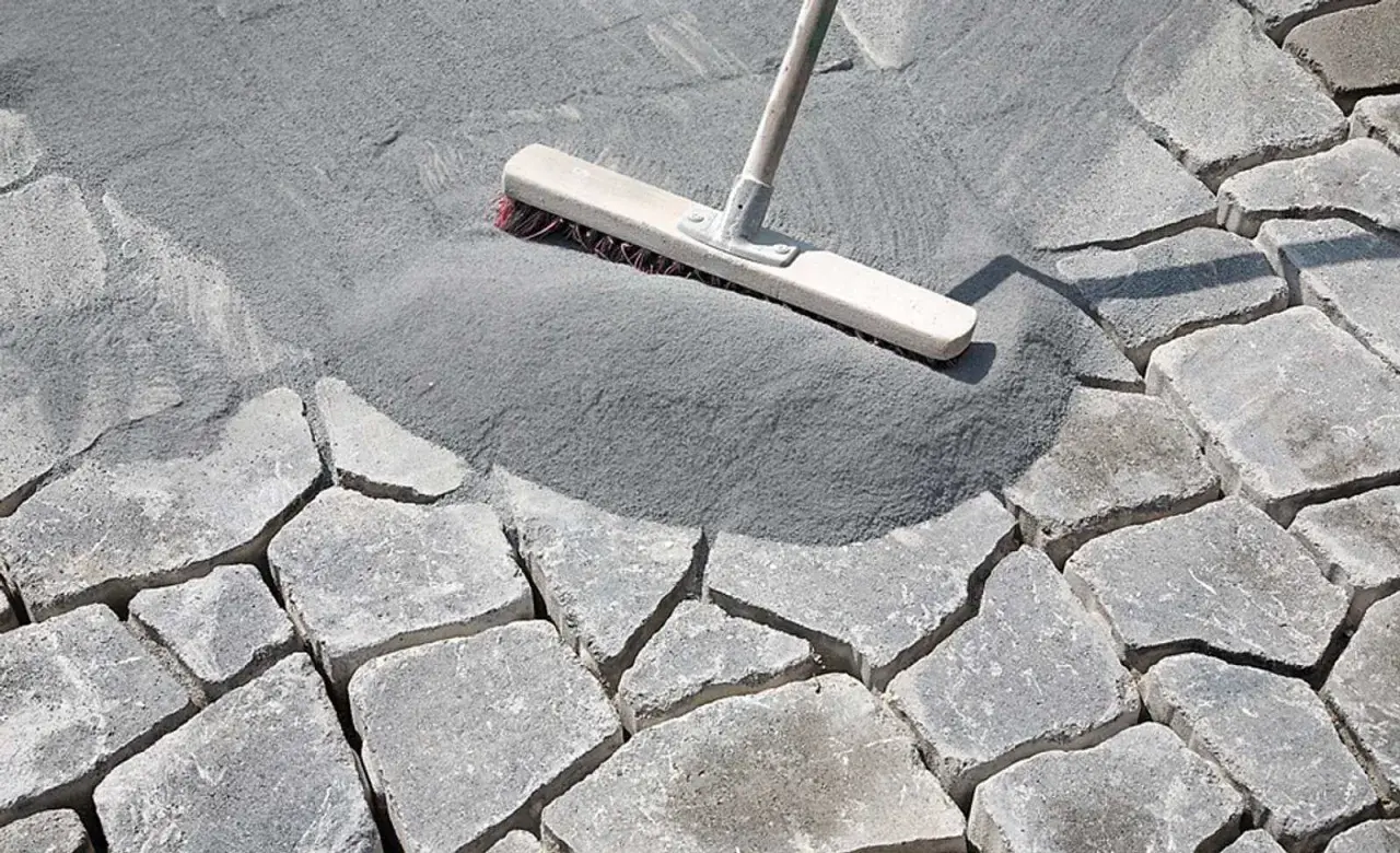 Besen verteilt feinen Fugensand auf Pflastersteinen. Der Sand dient als effektiver Fugensand gegen Unkraut und stabilisiert die Steine.