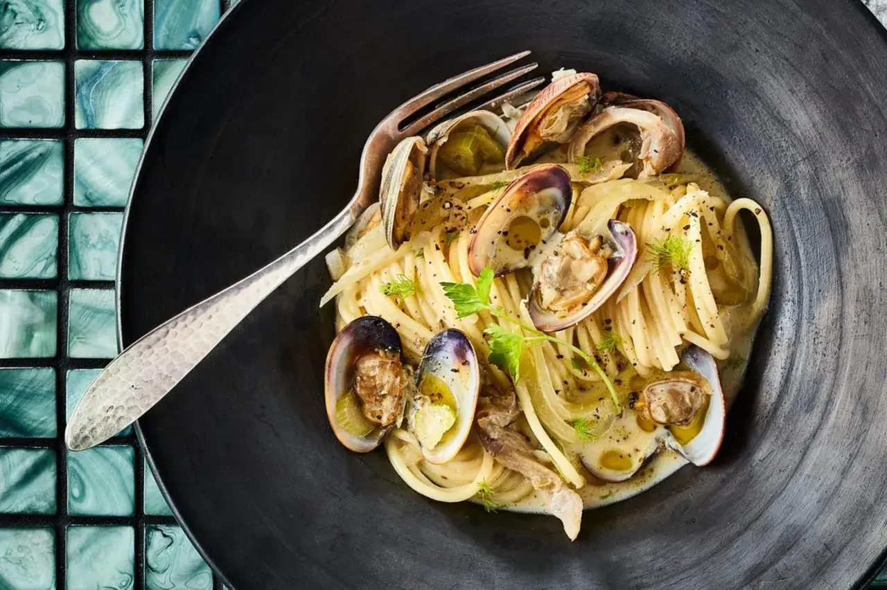 Spaghetti mit Venusmuscheln, ein köstliches Rezept. Serviert in einer schwarzen Schüssel mit einer Gabel.