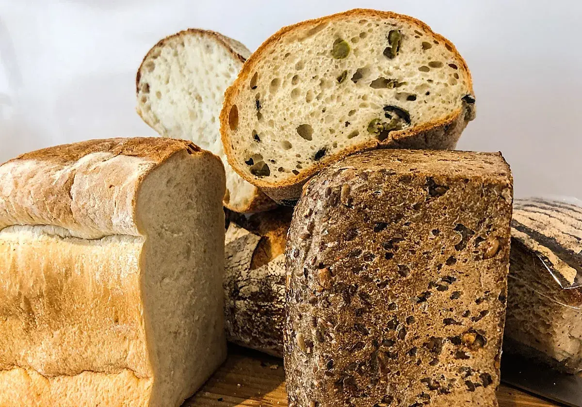 Variedad de panes artesanales, incluyendo un pan blanco esponjoso, un pan con aceitunas y un pan proteico con semillas.