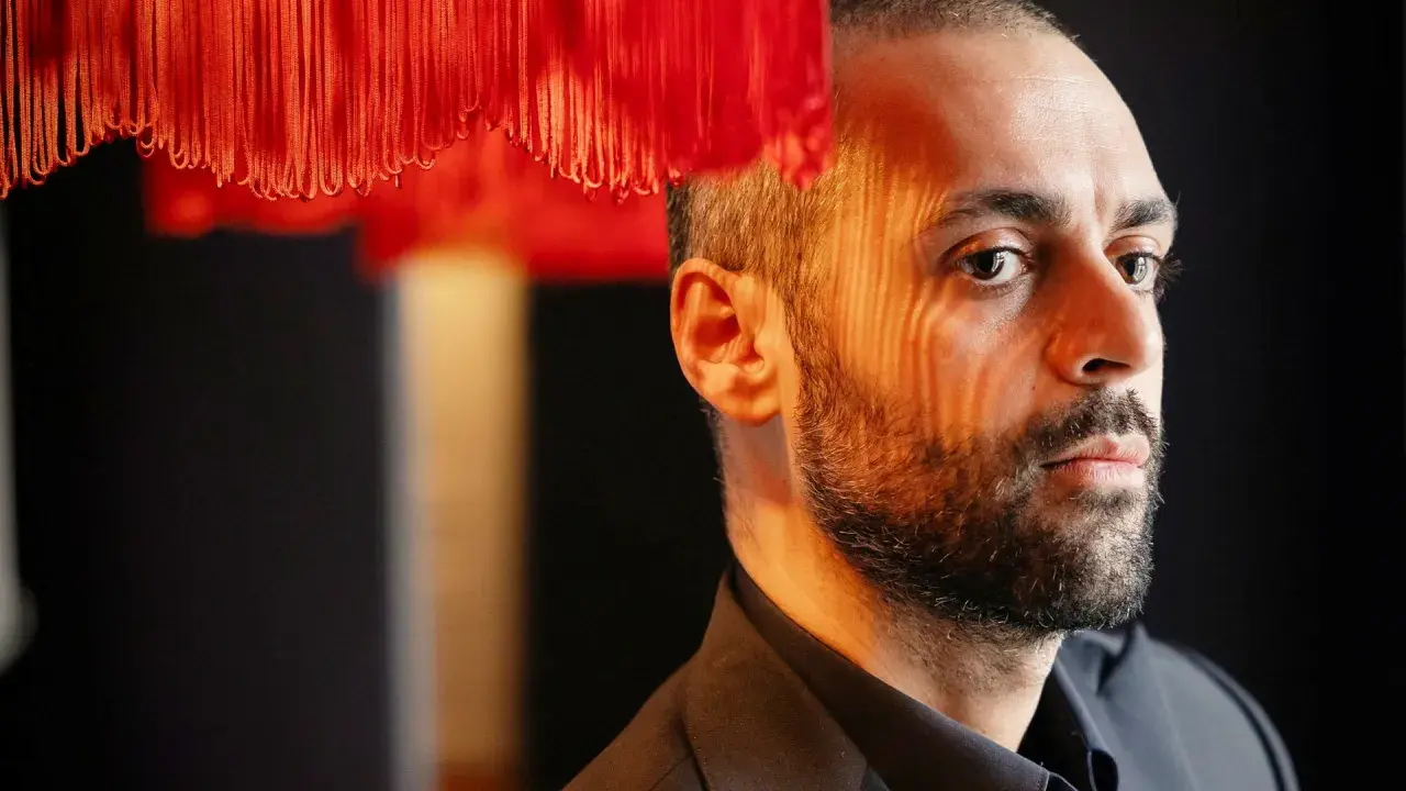 Ardalan Esmaili med ett intensivt uttryck, belyst av ett mönster av rött ljus från en lampa.