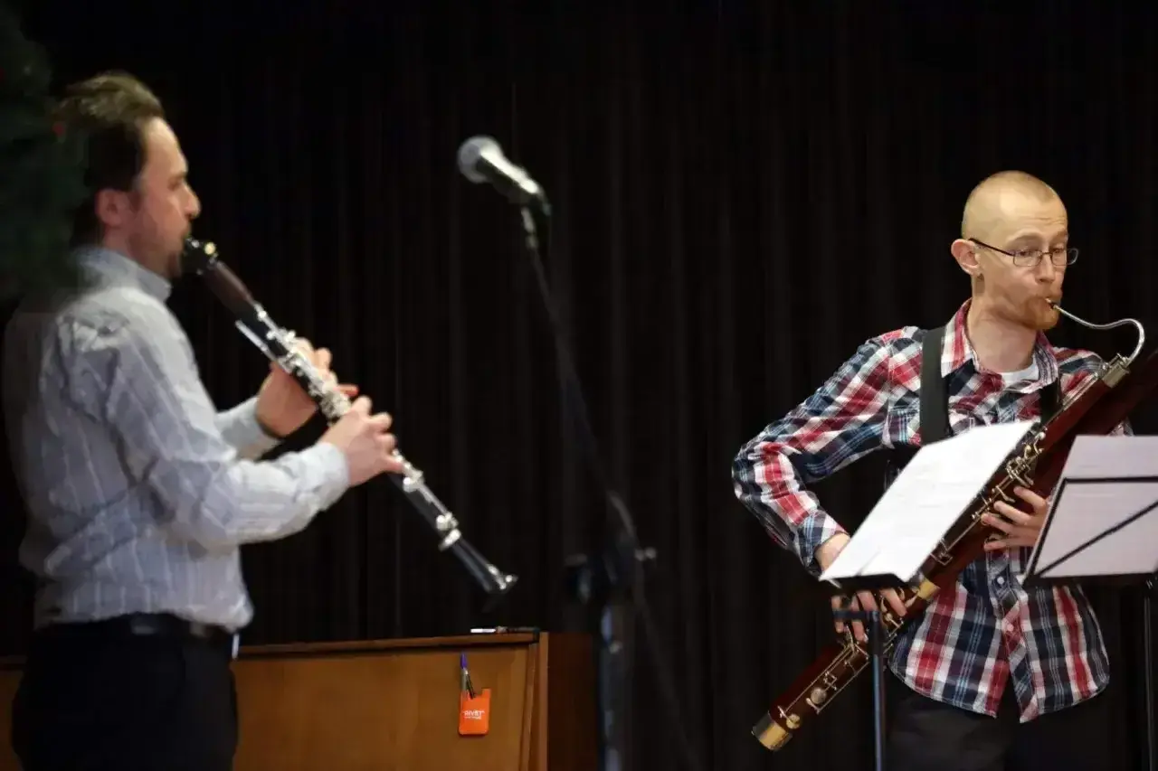 Dwóch muzyków gra na instrumentach dętych. Jeden na klarnecie, drugi na fagocie. Przed nimi stoją nuty na klarnet znane piosenki.