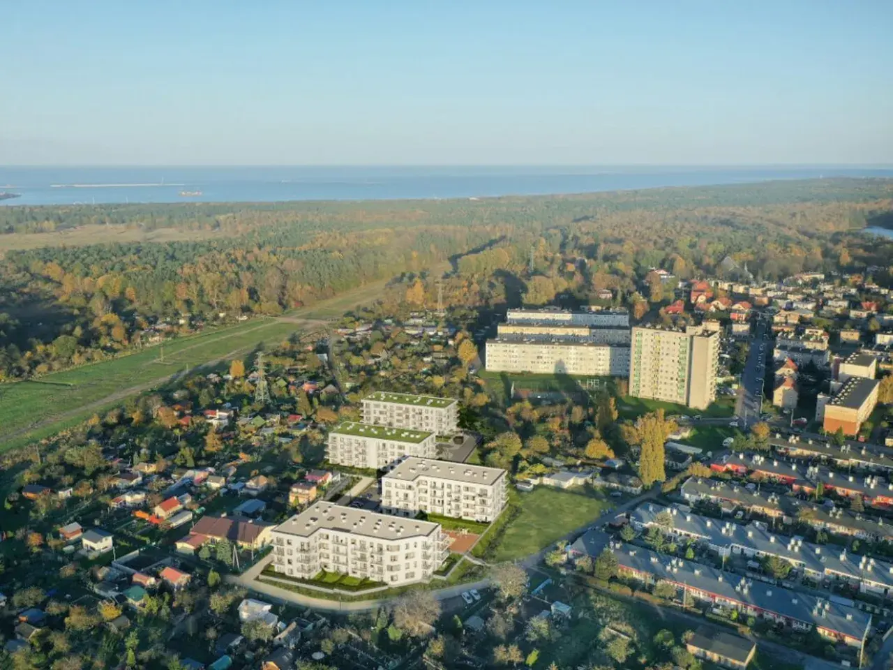 Nowoczesne bloki mieszkalne wyrastają pośród zieleni i domów jednorodzinnych, tworząc nowe młode stogi w krajobrazie. W tle morze i jesienny las.