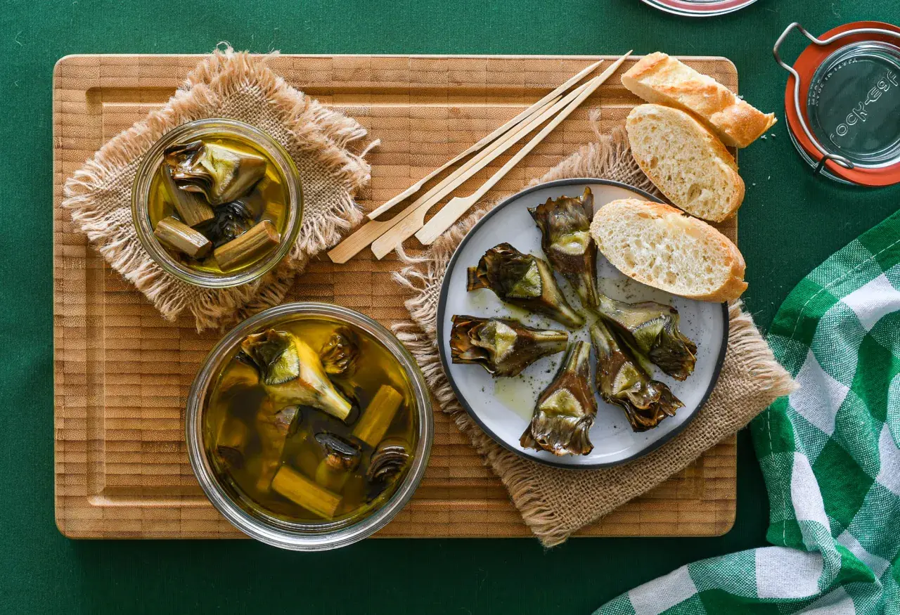 Deliciosas alcachofas confitadas en aceite de oliva, servidas con pan y palillos. Un manjar listo para disfrutar.