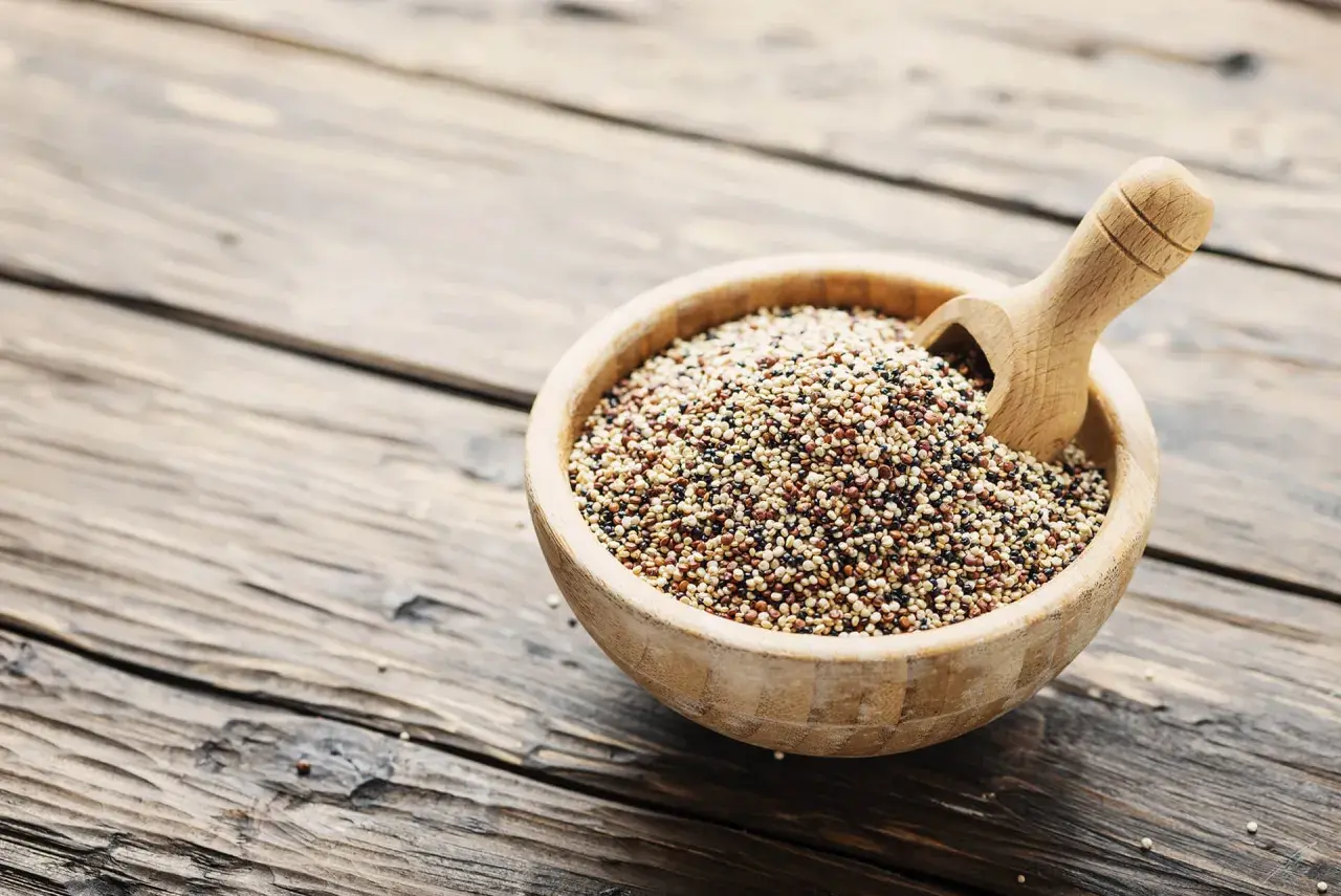 Ciotola di legno piena di quinoa tricolore, un legume nutriente, con un mestolo di legno.