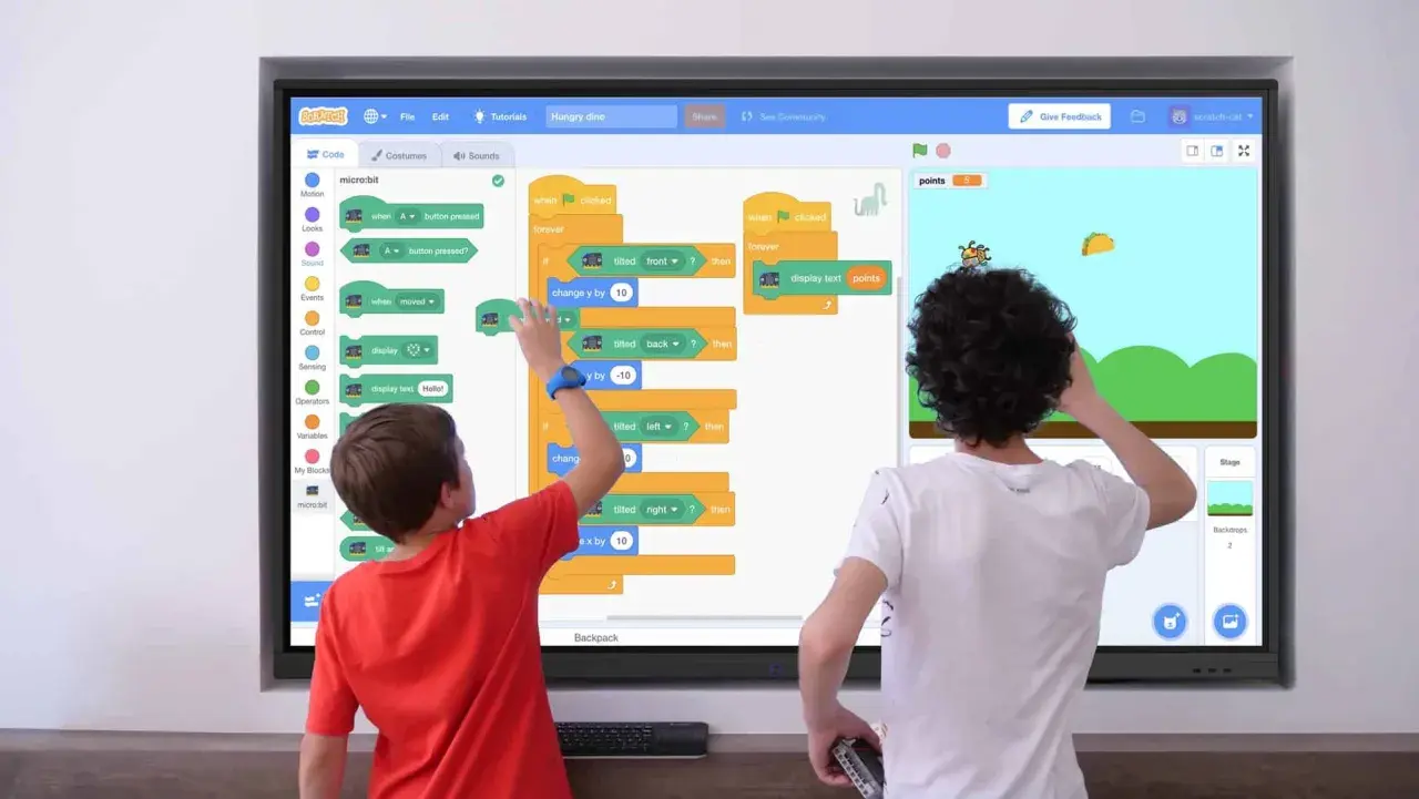 Zwei Kinder lernen Programmieren an einer digitalen Tafel in der Schule. Sie erstellen ein Spiel mit Scratch, das auf einem micro:bit basiert.