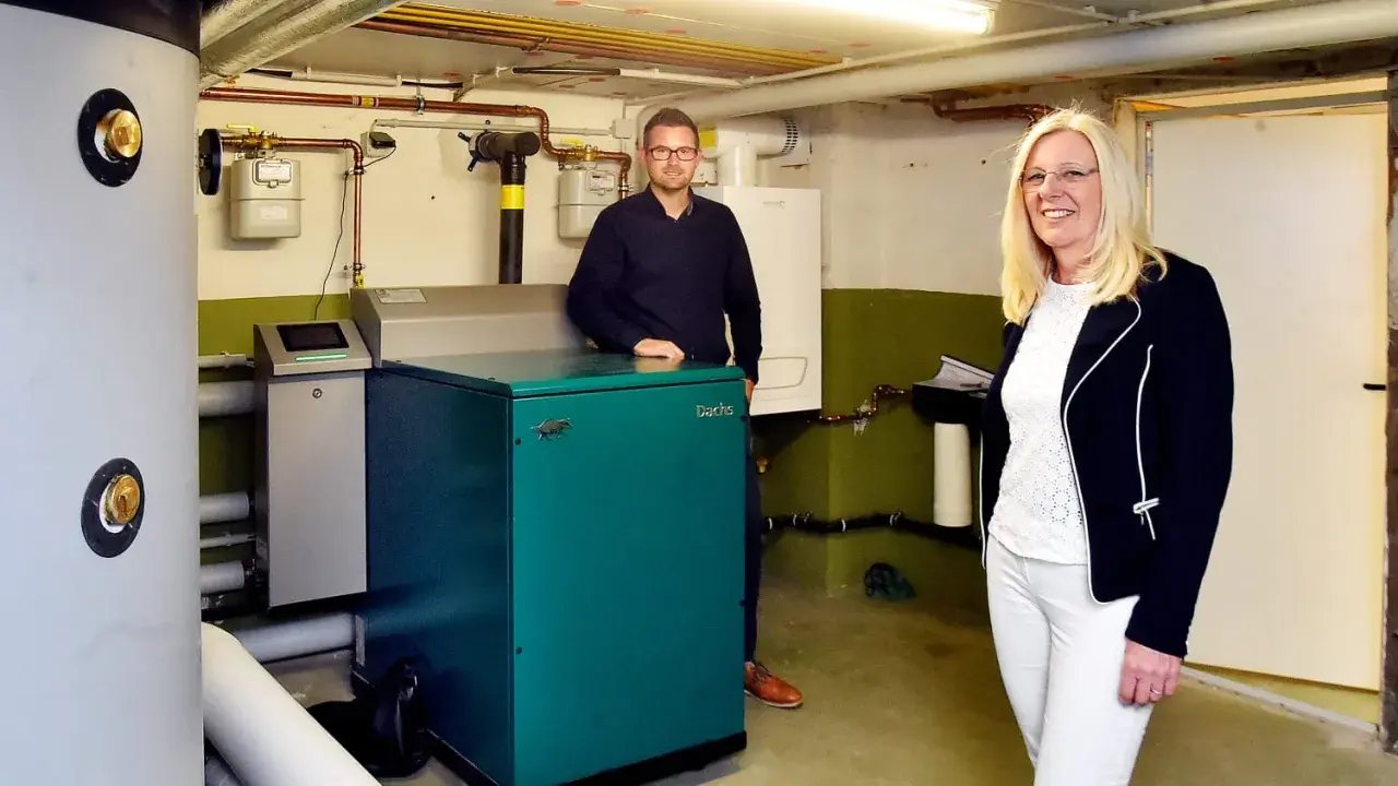 Ein Mann und eine Frau stehen neben einem grünen Nano BHKW-Gerät in einem Heizungsraum.