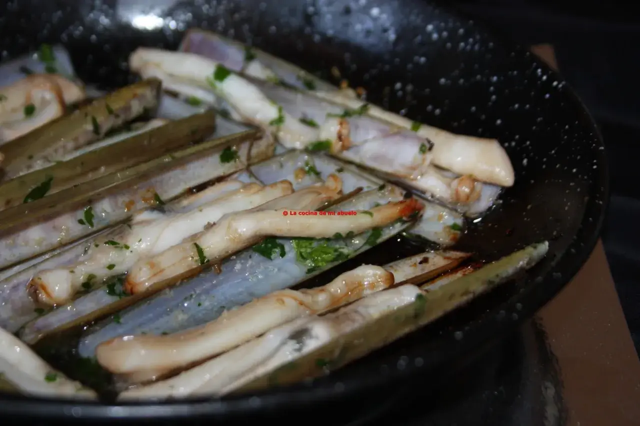Longueirón de Fisterra cocinándose en una sartén con perejil picado. Un plato marinero listo para disfrutar.