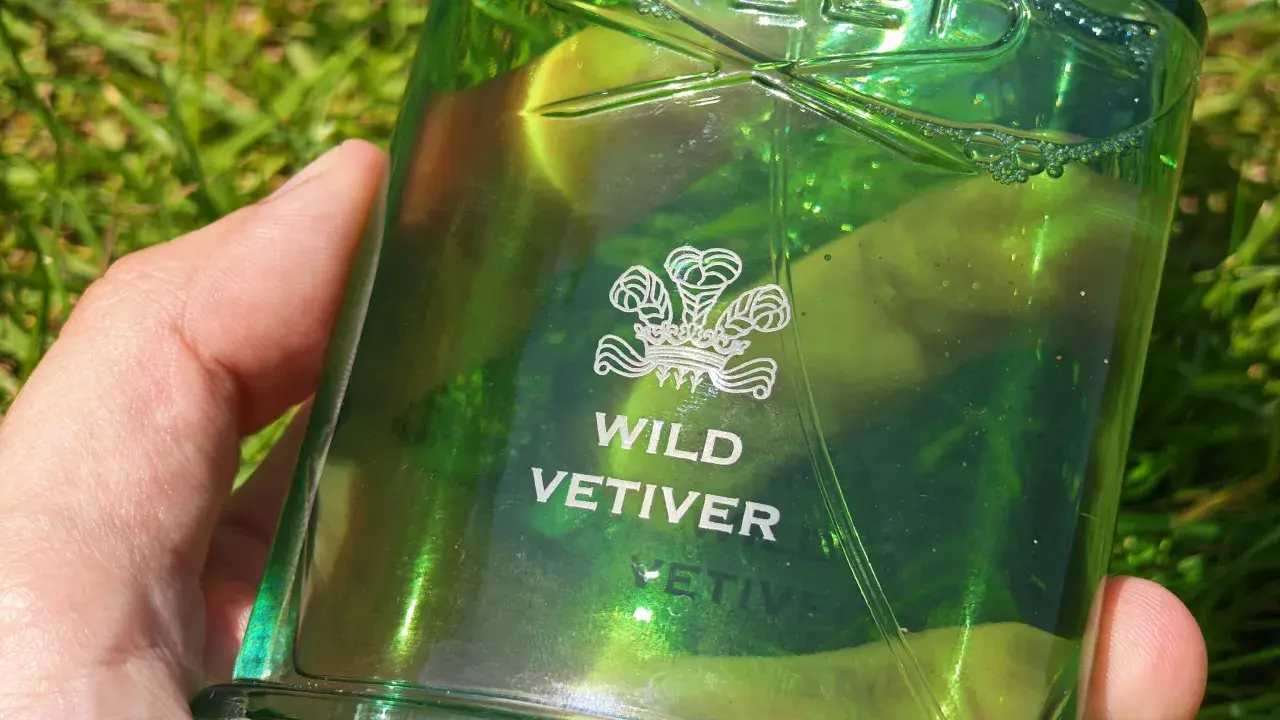 Zielona butelka perfum Creed Wild Vetiver w dłoni na tle trawy.