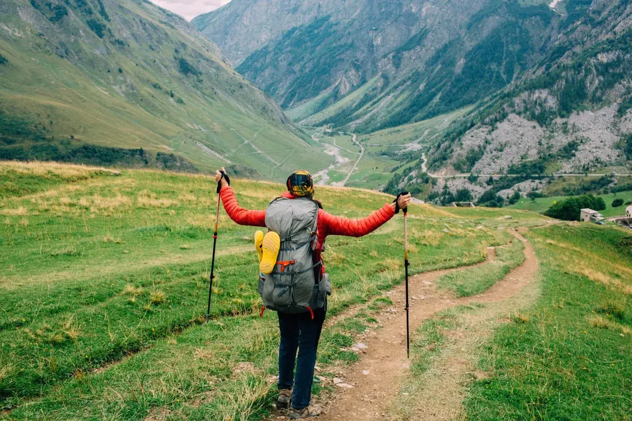 A hiker with a large backpack and trekking poles embraces the stunning alpine scenery on a self-guided tour du mont blanc.