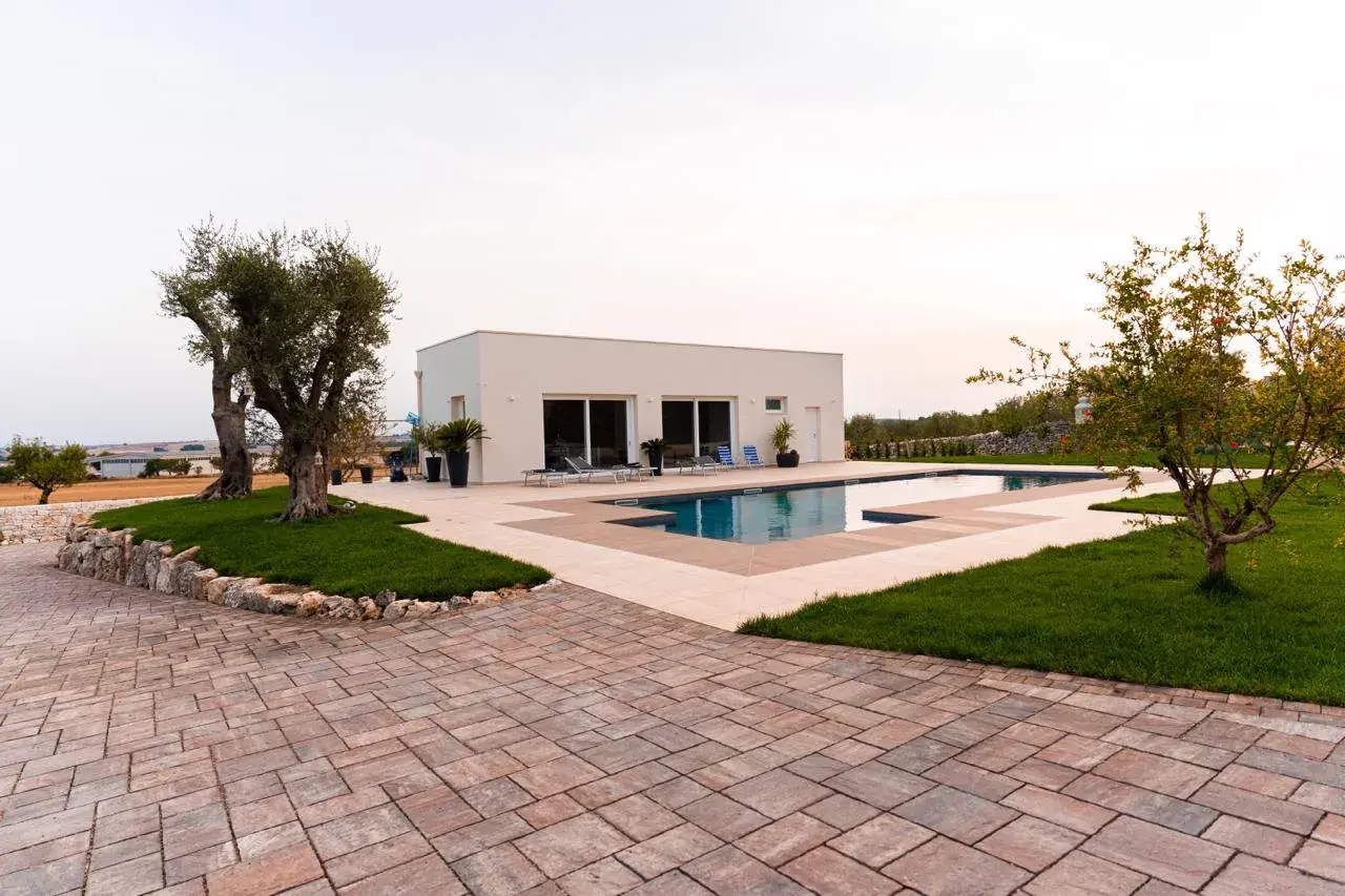 Pavimentazione esterna texture con blocchi di pietra color ruggine e beige, che circonda una piscina moderna e un prato verde.