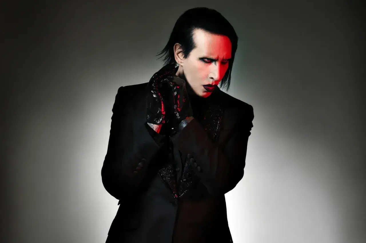 Marilyn Manson, wokalista zespołu, w czarnym garniturze i błyszczących rękawiczkach, z czerwonym światłem na twarzy.