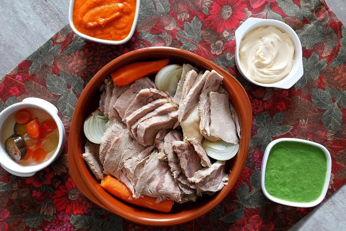 Un invitante bollito di carne, affettato e servito con carote, cipolle e tre salse: una rossa, una bianca e una verde.