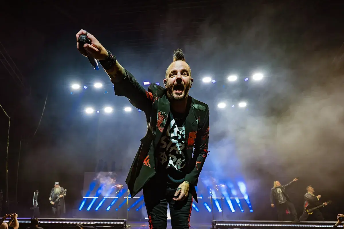 Wokalista Three Days Grace Polska z mikrofonem w dłoni, na scenie pełnej dymu i świateł.