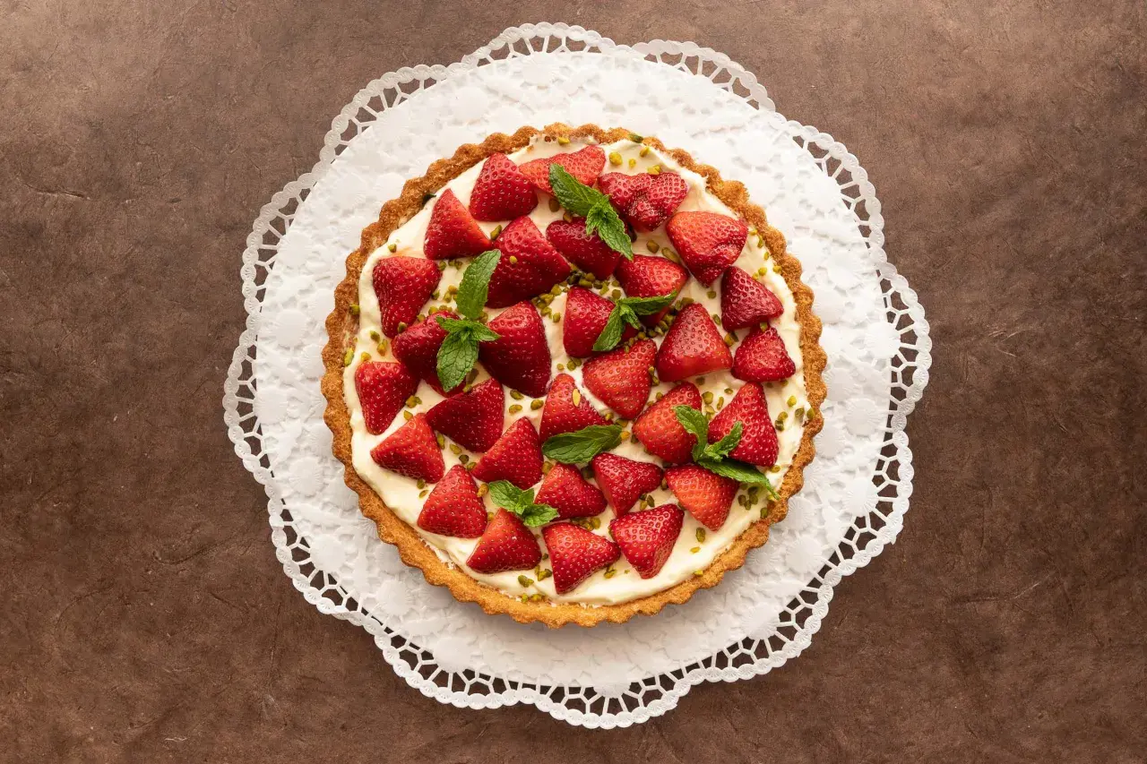 Ein köstlicher Erdbeerkuchen mit Pudding, garniert mit frischen Erdbeeren und Minze, auf einer zarten Papierspitze.