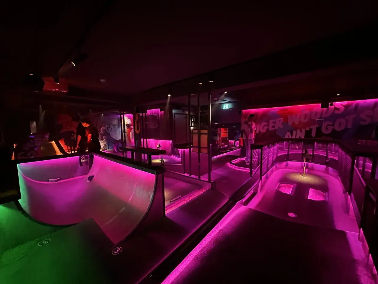 En neonupplyst minigolfbana i Göteborg med rosa och grönt ljus. En person står vid en bana.