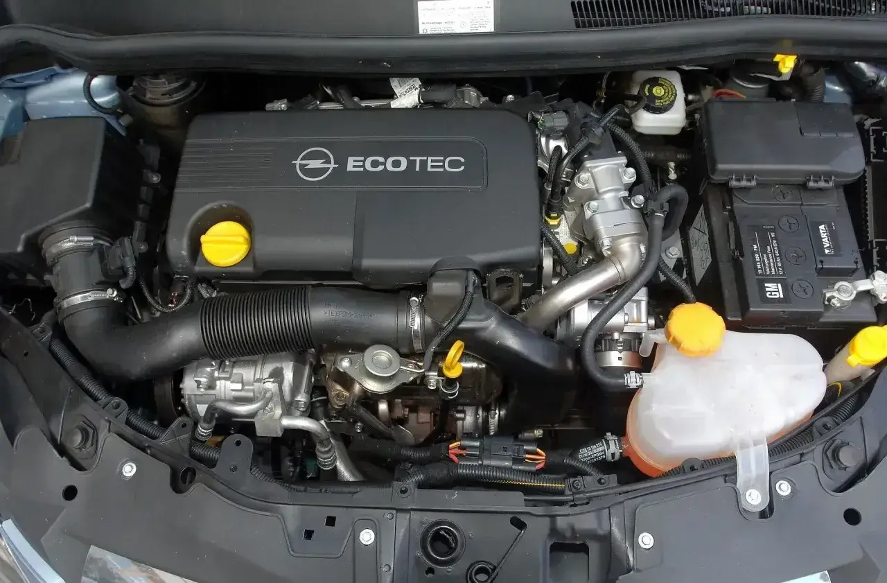 Silnik Opel Corsa D 1.2 benzyna. Widoczny jest czarny dekiel z napisem Ecotec, akumulator Varta oraz zbiornik płynu chłodniczego.