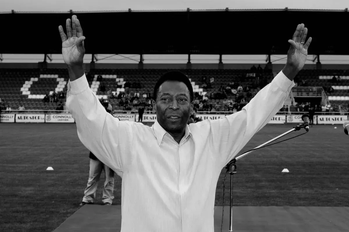 Pelé z uniesionymi rękami na tle stadionu. Jego wzrost i charyzma zawsze robiły wrażenie.