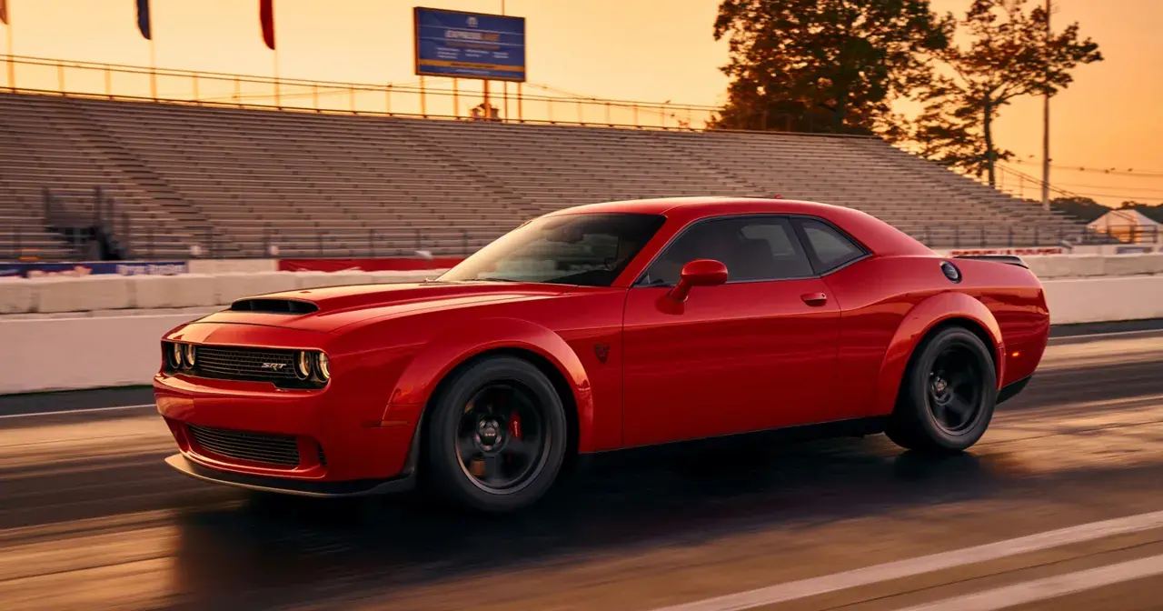 Czerwony Dodge Challenger SRT pędzi po torze wyścigowym podczas zachodu słońca, z trybunami w tle.