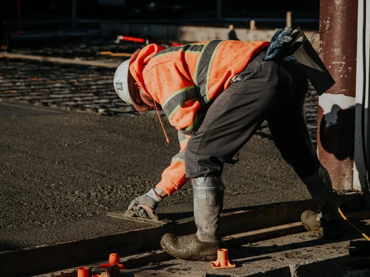 Robotnik w pomarańczowej kamizelce wygładza świeżą wylewkę. Zastanawiasz się, ile worków wylewki na 1m2 potrzeba?