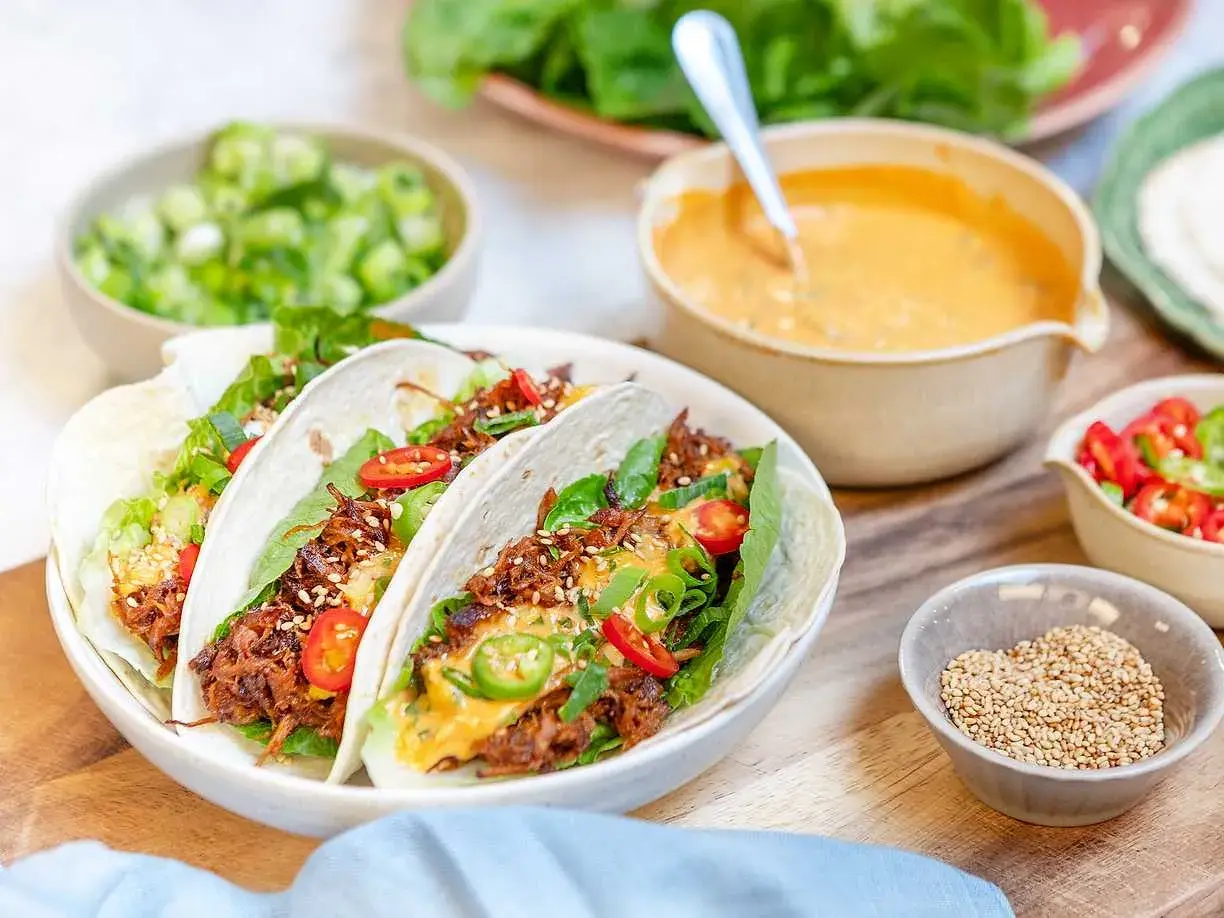 Tacos med koreansk pulled pork, toppade med sallad, chili och sesamfrön. Serveras med en krämig sås och färska grönsaker.