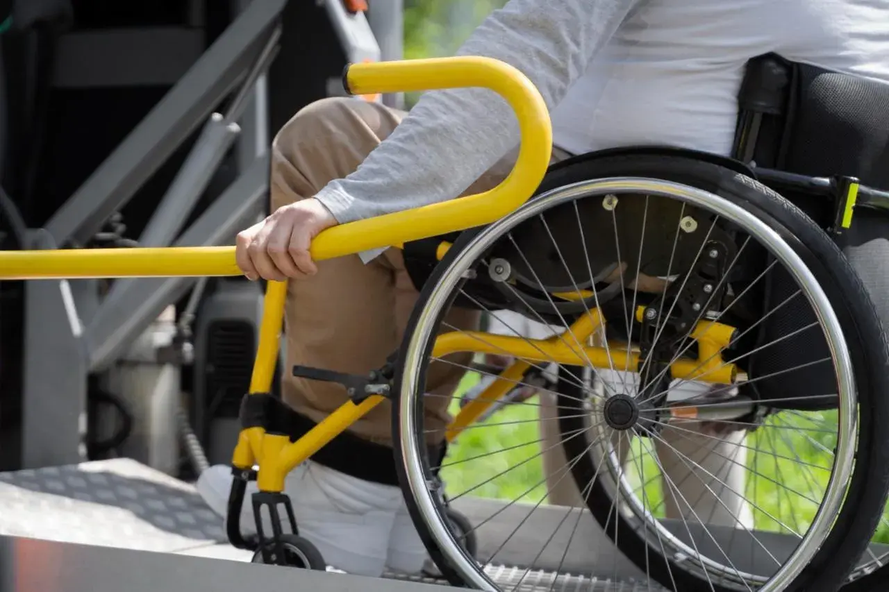 Persona in sedia a rotelle si aggrappa a un corrimano giallo, suggerendo un noleggio auto con legge 104 per maggiore accessibilità.