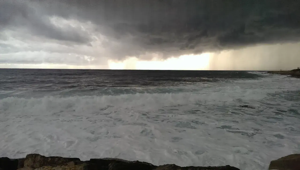 Burzowe niebo nad wzburzonym morzem w Pafos. Grudzień przynosi dramatyczne chmury i deszcz na horyzoncie.