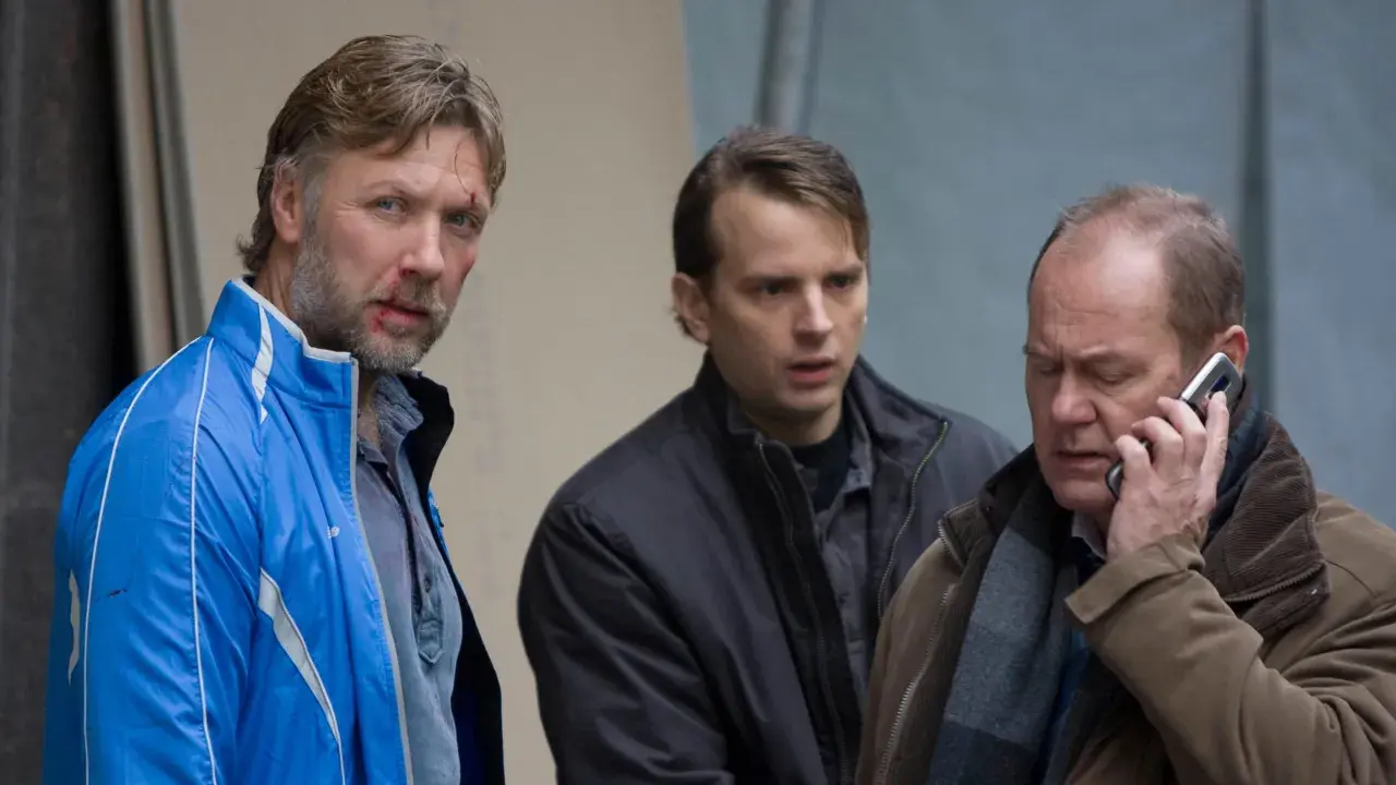 Tomas Fryk, med blodfläckar i ansiktet, står med två andra män. En pratar i telefon.