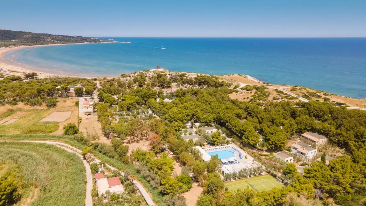 Vista aerea della baia della Tufara con mare azzurro, spiaggia dorata, pineta lussureggiante, piscina e campo da tennis.