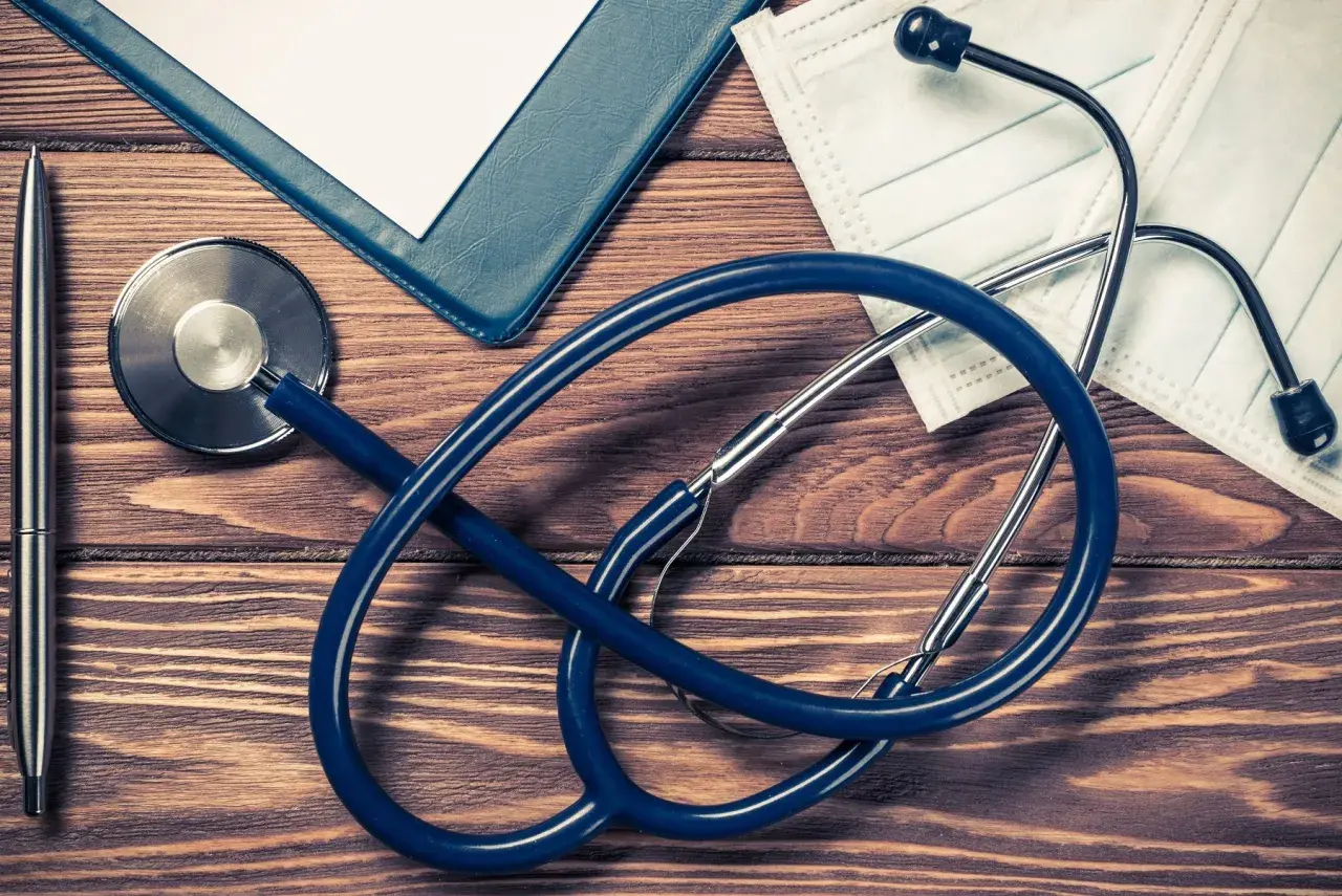 Stetoscopio, penna, cartella e mascherina su tavolo di legno. Preparativi per aprire studio medico in appartamento.