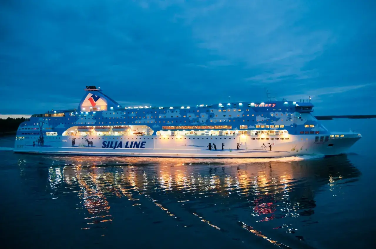 Prom Silja Line Galaxy płynie po wodzie o zmierzchu, odbijając światła w mroku. Podróż z Rygi do Helsinek zaczyna się!
