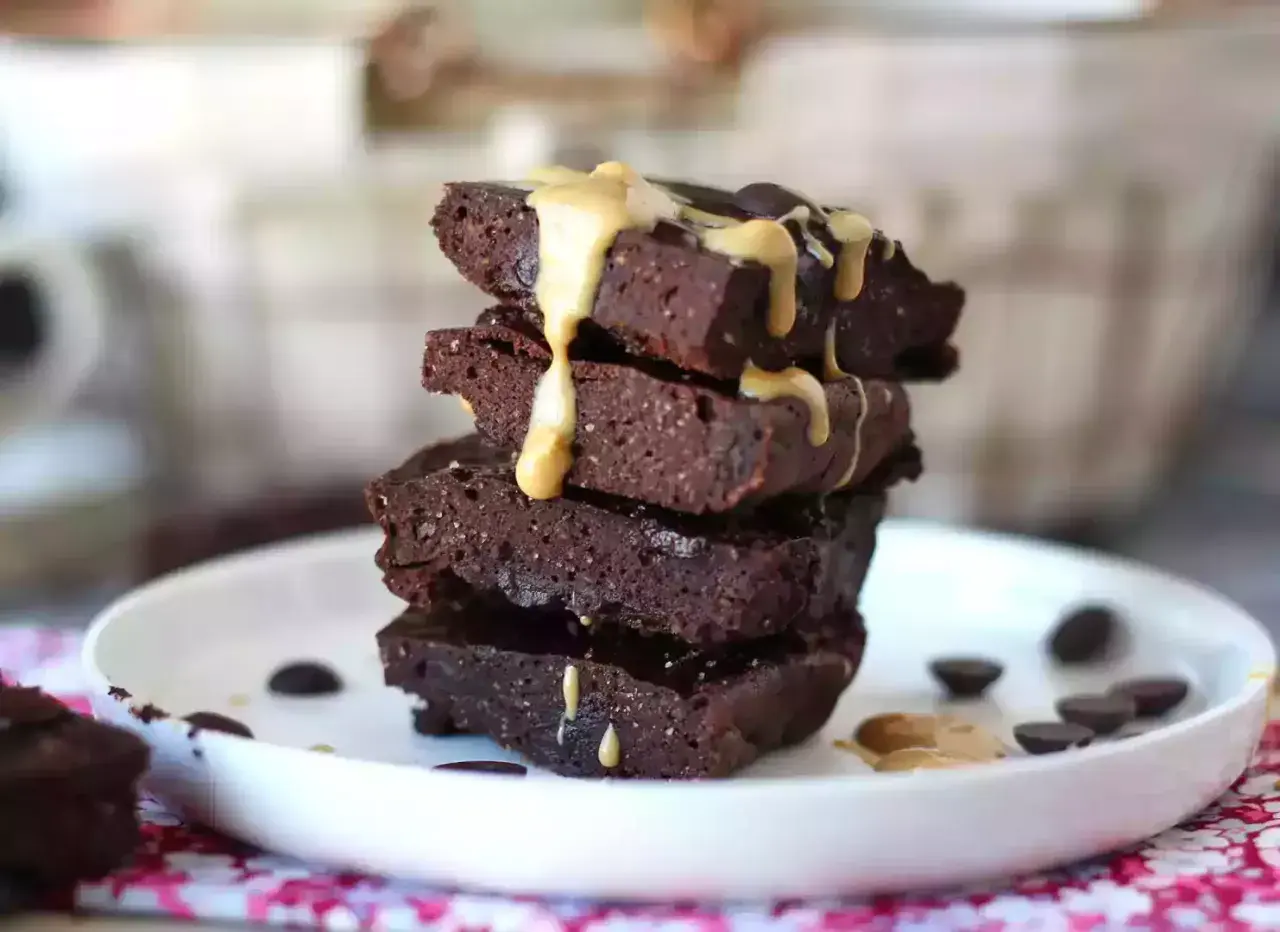 En stapel mörka protein brownies med en krämig topping och chokladknappar på en vit tallrik.