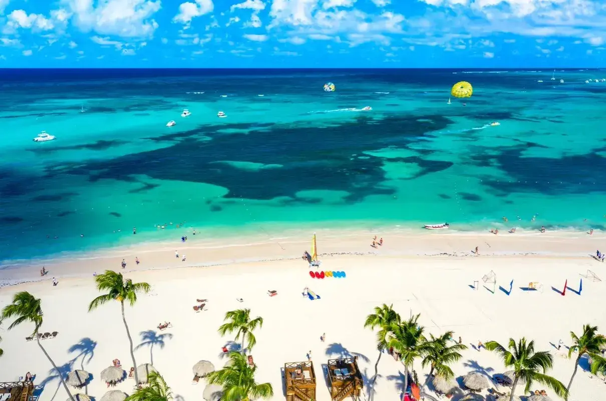 Rajska plaża na Dominikanie z turkusową wodą, palmami i ludźmi cieszącymi się słońcem. Sprawdź atrakcyjne dominikana ceny na wakacje!