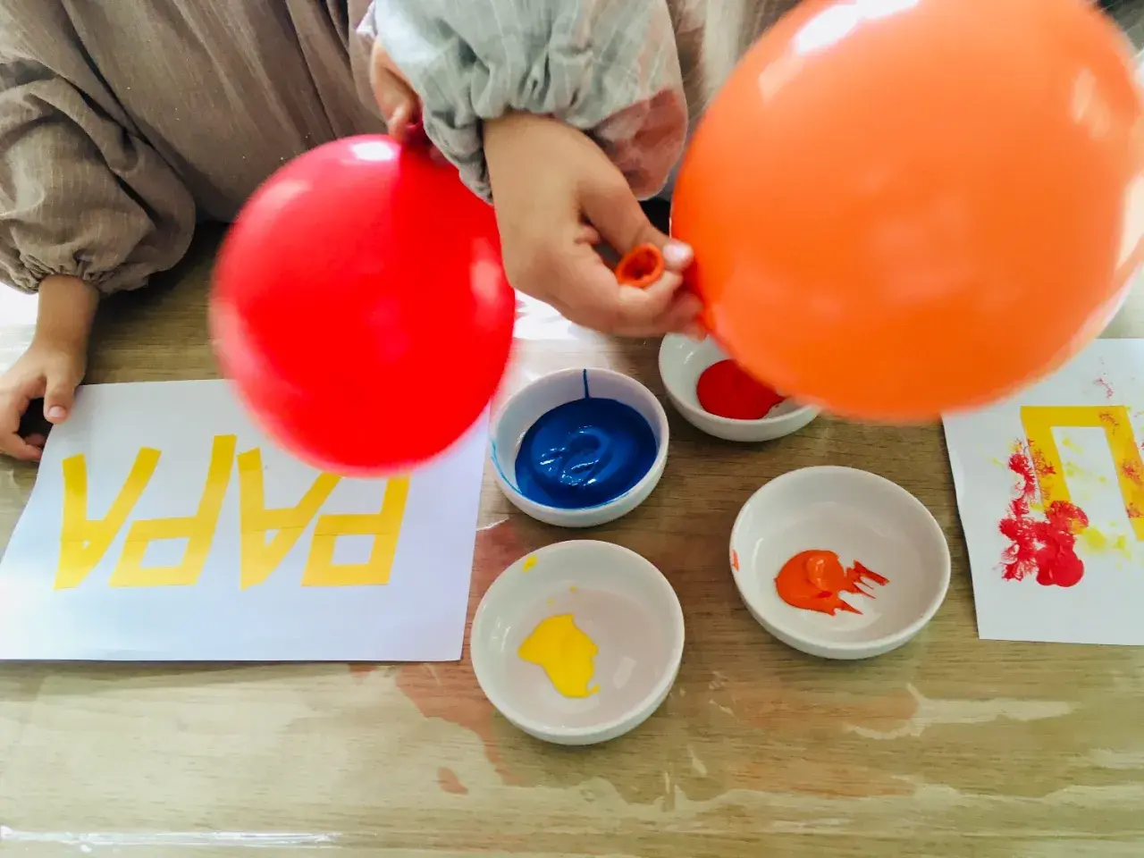 Kinder malen mit Luftballons bunte Muster auf Papier. Rote und orange Luftballons werden in Farbe getaucht.